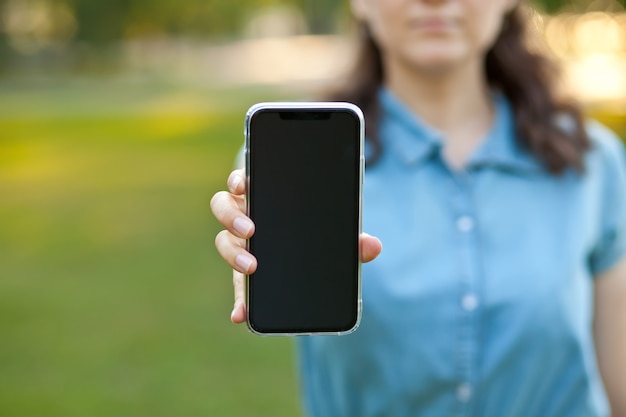 Mujer sosteniendo y mostrando la pantalla del teléfono inteligente móvil en blanco