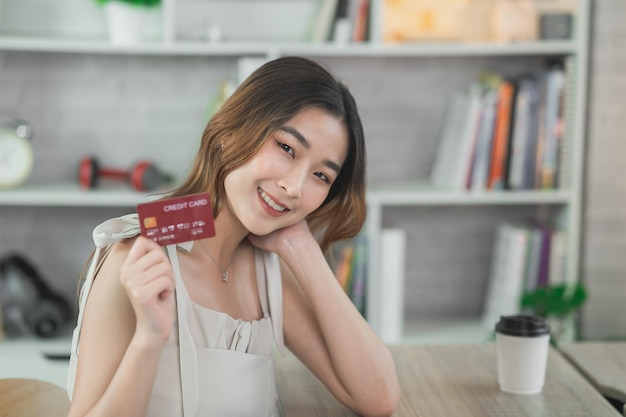 Mujer sosteniendo mostrando tarjeta de crédito para comprar en línea mujer asiática que trabaja en casa Compras en línea comercio electrónico banca por Internet gastar dinero trabajando desde el concepto de hogar