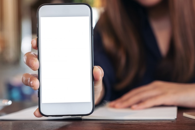 Una mujer sosteniendo y mostrando un teléfono móvil blanco con pantalla en blanco en el café