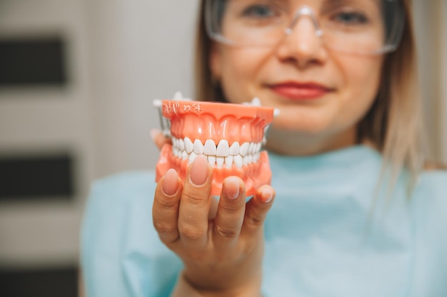 Mujer sosteniendo una muestra de diente o dentadura en el dentista. concepto de medicina y odontología.