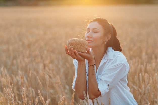 Mujer sosteniendo pan de trigo casero en manos en campo de trigo al atardecer.