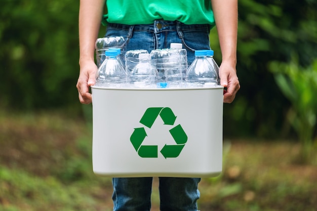 Una mujer sosteniendo una papelera de reciclaje con botellas de plástico al aire libre