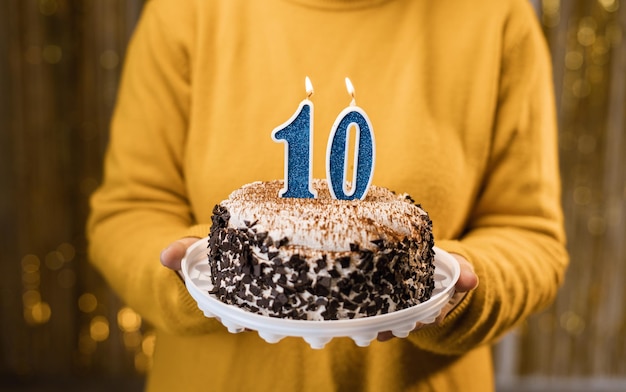 Mujer sosteniendo pastel de cumpleaños con velas encendidas número 10 contra un fondo decorado de cerca Celebra el cumpleaños en casa