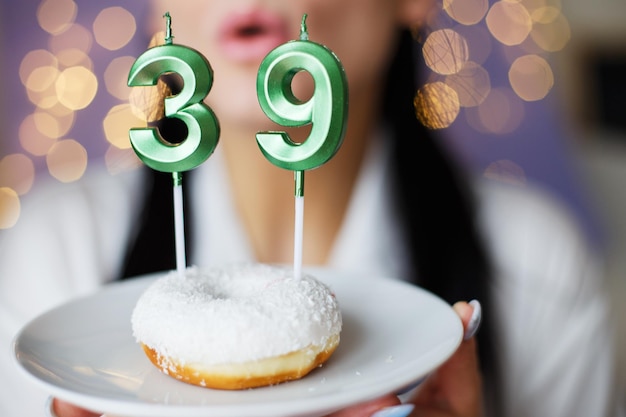 Mujer sosteniendo un pastel con las velas número 39 sobre un fondo bokeh borroso festivo