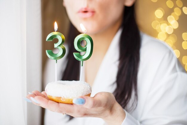 Mujer sosteniendo un pastel con las velas número 39 sobre un fondo bokeh borroso festivo