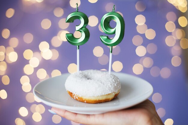 Mujer sosteniendo un pastel con las velas número 39 sobre un fondo bokeh borroso festivo