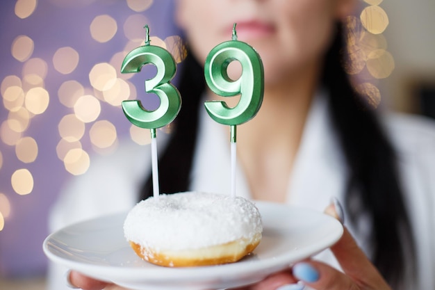 Mujer sosteniendo un pastel con las velas número 39 sobre un fondo bokeh borroso festivo