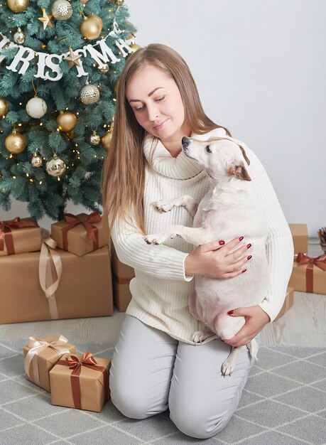 Mujer sosteniendo perro cerca de cajas de regalo y árbol de Navidad