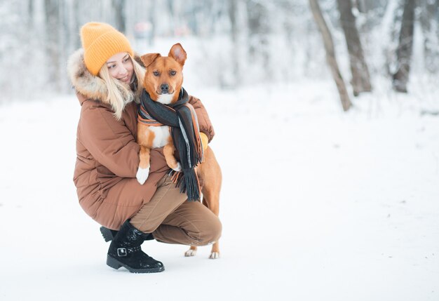 Mujer sosteniendo perro mestizo rojo en bufanda en bosque de invierno