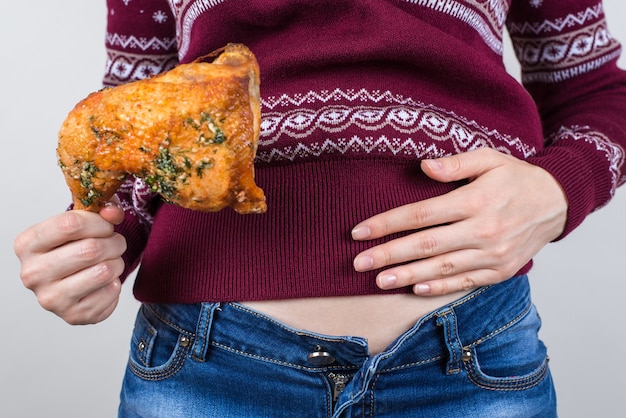 Mujer sosteniendo la pierna de pollo frito en una mano y la otra mano sobre el estómago lleno