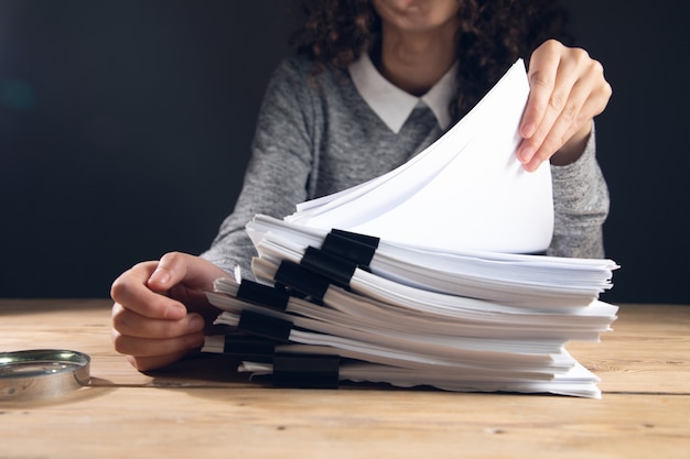 Foto mujer sosteniendo una pila de archivos con lupa sobre la mesa