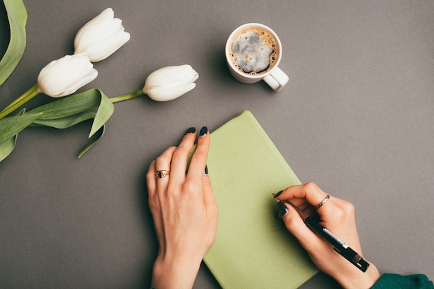 Mujer sosteniendo planificador o agenda cerca de tulipanes blancos y café de la mañana