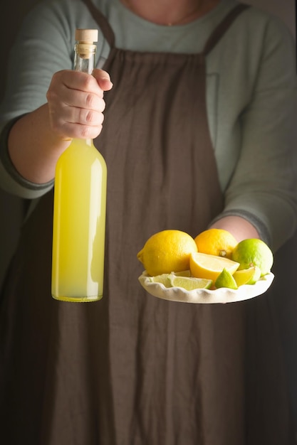 Mujer sosteniendo un plato de limón y lima y una botella de bebida casera