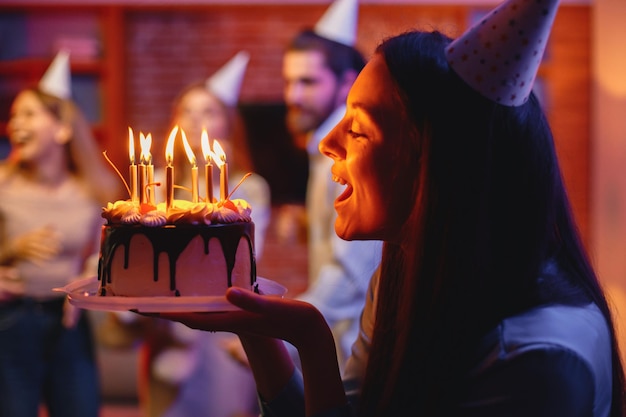 Mujer sosteniendo un plato con pastel de cumpleaños frente a personas borrosas en una fiesta