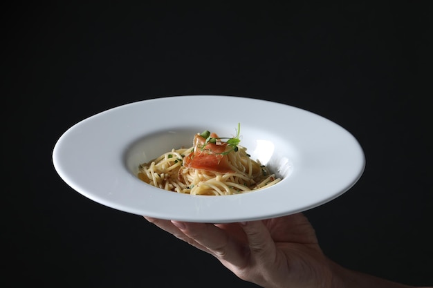 Mujer sosteniendo plato de sabrosos espaguetis con prosciutto y microgreens sobre fondo negro primer plano Exquisita presentación de plato de pasta