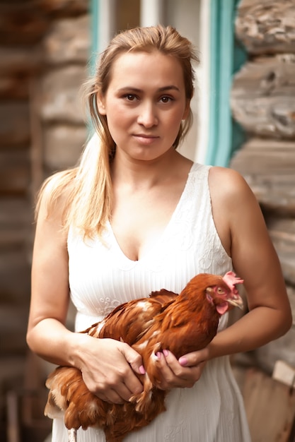 Mujer sosteniendo un pollo en un gallinero. Animales de granja.