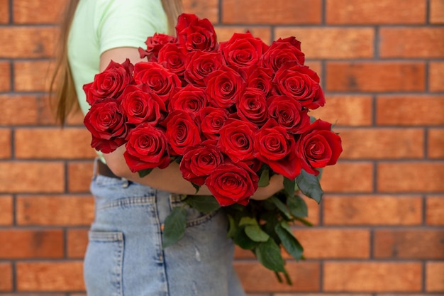 Mujer sosteniendo ramo de lujo de rosas rojas frescas contra el fondo de la pared de ladrillo