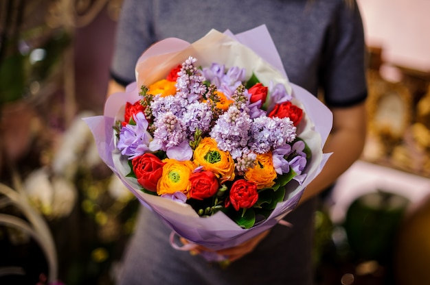 Mujer sosteniendo un ramo de tulipanes rojos, lila y ranúnculo naranja