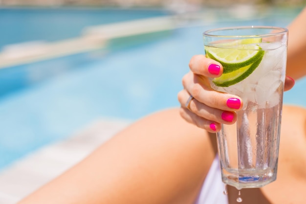 Mujer sosteniendo refrescante bebida fría mientras toma el sol junto a la piscina