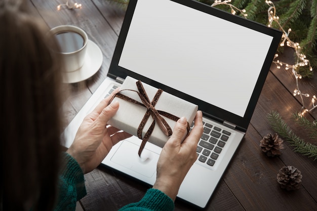 Mujer sosteniendo regalo y escribiendo por laptop en casa interior