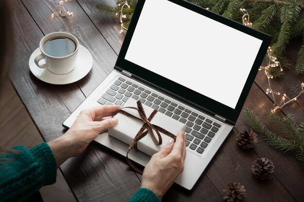 Mujer sosteniendo regalo y escribiendo por laptop.