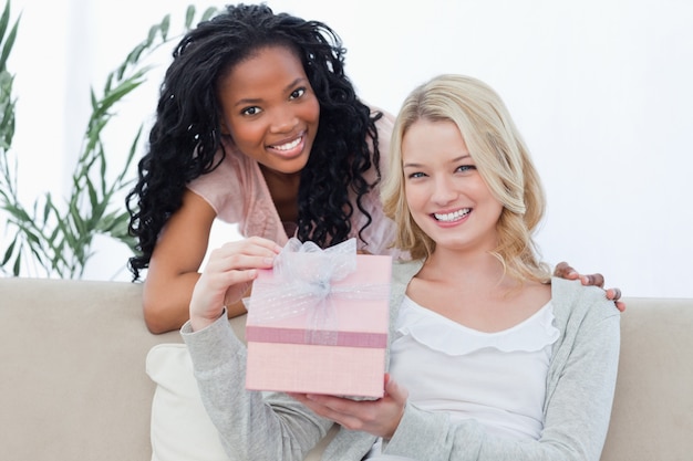 Una mujer sosteniendo un regalo sonríe a la cámara con su amiga.