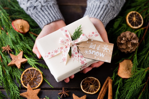 Mujer sosteniendo regalos de Navidad sobre una mesa de madera.