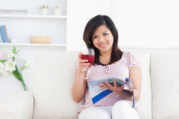 Mujer sosteniendo una revista mientras sostiene un vaso de vino tinto