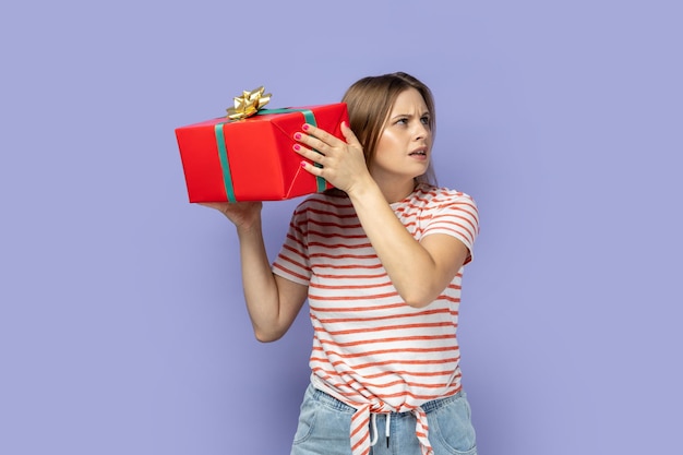Foto mujer sosteniendo y sacudiendo una caja de regalo roja interesada en qué regalo le dieron sus amigos