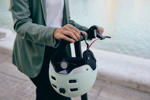 Mujer sosteniendo un scooter eléctrico mientras va a trabajar en la ciudad