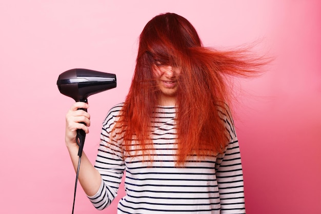 Mujer sosteniendo un secador de pelo sobre un fondo rosa