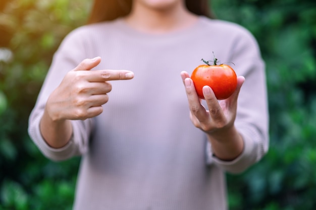 Una mujer sosteniendo y señalando con el dedo un tomate fresco