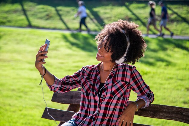 Mujer sosteniendo smartphone tomando foto selfie y de pie en el parque