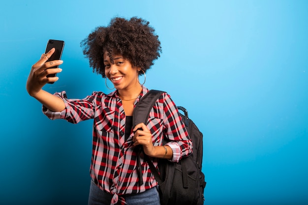 Mujer sosteniendo smartphone tomando foto selfie sobre el fondo azul.