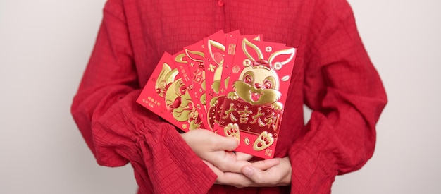 Mujer sosteniendo un sobre rojo chino con un conejo dorado y una palabra de bendición regalo de dinero para las felices vacaciones del Año Nuevo Lunar La oración china significa felicidad saludable Afortunado y rico