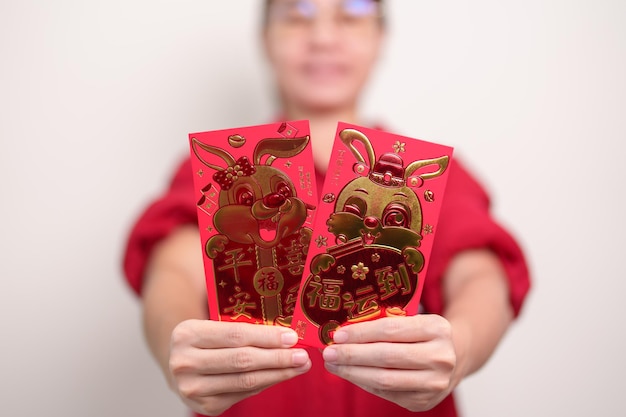 Mujer sosteniendo un sobre rojo chino con un conejo dorado y una palabra de bendición regalo de dinero para las felices vacaciones del Año Nuevo Lunar La oración china significa felicidad saludable Afortunado y rico