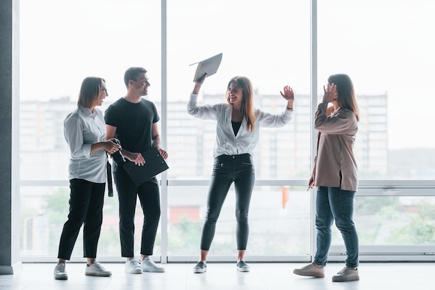 Mujer sosteniendo su cámara profesional Grupo de empresarios en ropa formal de pie en el interior cerca de una gran ventana