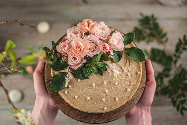 Mujer sosteniendo en sus manos un hermoso pastel de mousse crudo decorado con flores de ternura