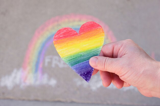 Mujer sosteniendo en sus palmas un corazón de papel pintado en los colores del arco iris del arco iris de la comunidad lgbt, tiza en el pavimento, concepto de orgullo del mes - arte temporal