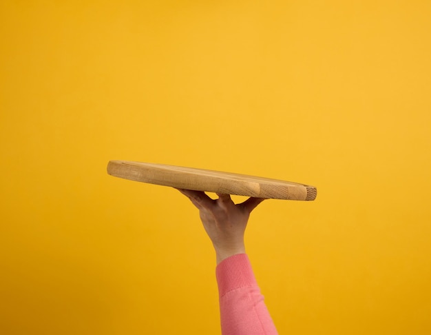 Mujer sosteniendo una tabla de pizza de madera redonda vacía en la parte del cuerpo de la mano sobre un fondo amarillo