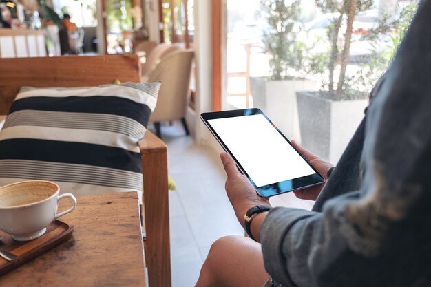 Mujer sosteniendo tablet pc negro con pantalla en blanco con taza de café en la mesa de madera en el café