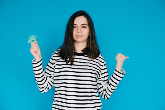 Mujer sosteniendo tarjeta de crédito apuntando con el pulgar en el espacio vacío mujer expresando confianza y