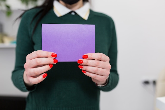Mujer sosteniendo una tarjeta púrpura en blanco frente a ella