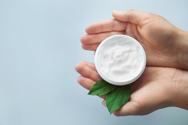 Foto mujer sosteniendo tarro con crema y hojas verdes sobre fondo blanco.