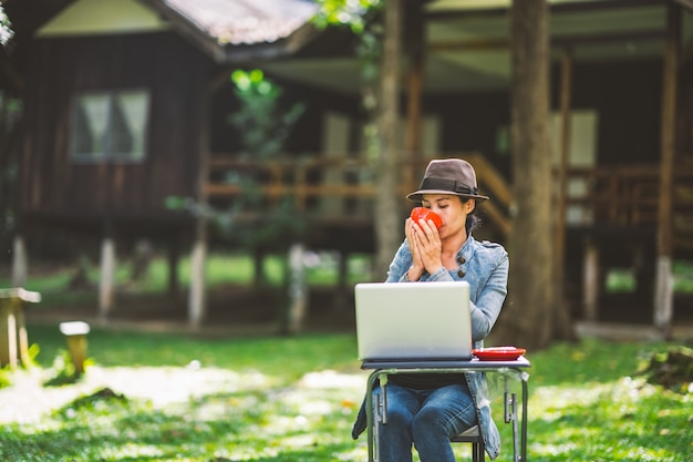 Mujer sosteniendo una taza de café y bebiendo en la mañana y trabajando en la computadora portátil