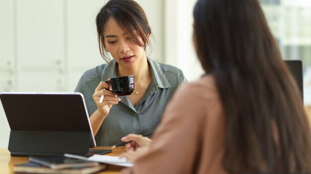 Mujer sosteniendo una taza de café y hablando con su compañero de trabajo mientras se reúne en su proyecto