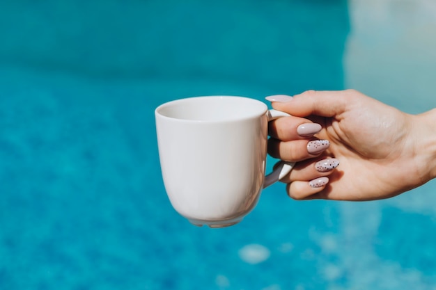 Mujer sosteniendo una taza de café con leche junto a la piscina