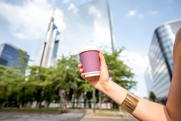 Mujer sosteniendo una taza de café para llevar con espacio de copia al aire libre en el fondo de la ciudad moderna