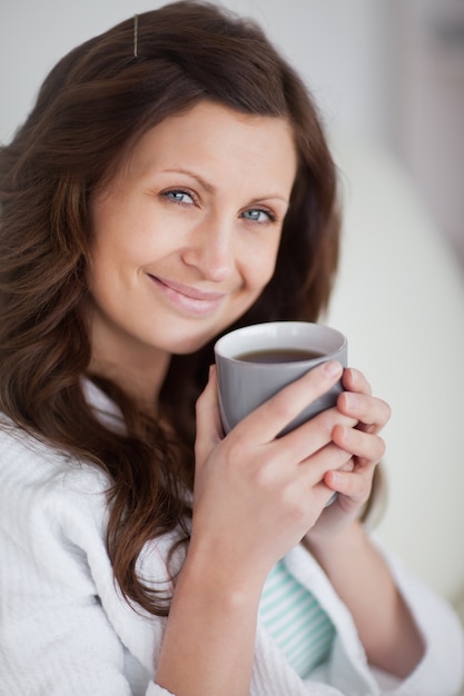 Mujer sosteniendo una taza de café mientras mira a la cámara