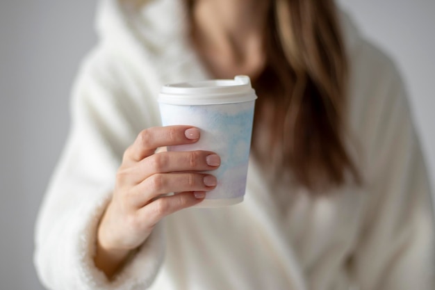 Una mujer sosteniendo una taza de café de plástico con un delicado dibujo de acuarela en la mano en casa